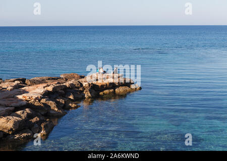 CYPRUS - APRIL 15, 2018: Small remote rocky bay. People enjoy azure sea. Stock Photo