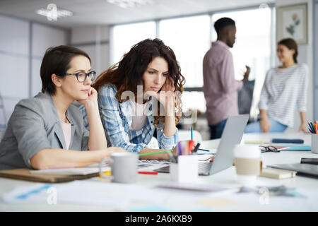 Portrait of two young businesswomen looking at laptop screen while planning creative project in publishing agency, copy space Stock Photo