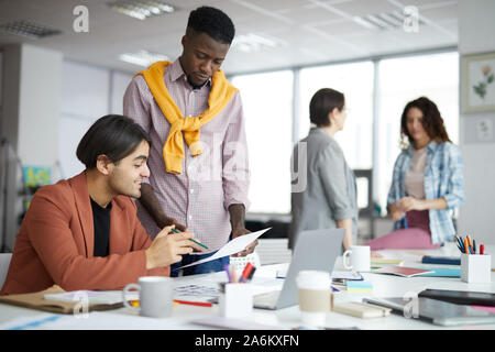 Diverse team on creative young people discussing startup project in modern office, focus on two ethnic men in foreground, copy space Stock Photo