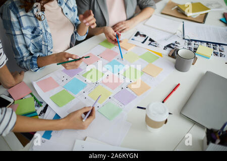 High angle view of creative team planning startup project on table, focus on hands pointing at colorful sticky notes during meeting, copy space Stock Photo