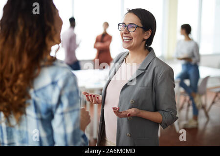 Waist up portrait of young businesswoman laughing happily while talking to colleague in office, copy space Stock Photo