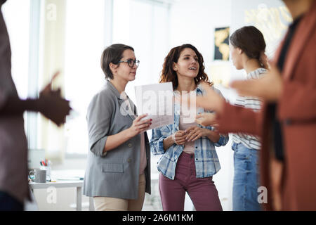 Image of crowded office with focus on three young businesswomen discussing creative project, copy space Stock Photo