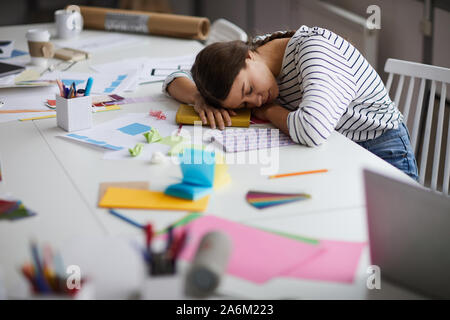 Side view portrait of young woman sleeping at desk exhausted from working or studying, copy space Stock Photo