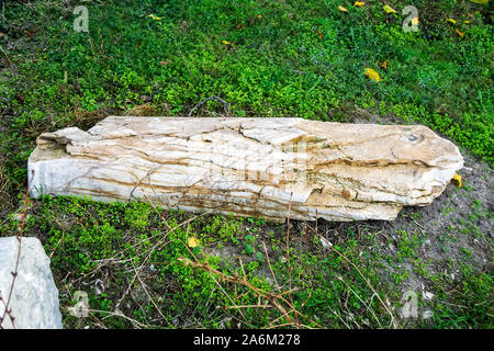 Fragment of a partially destroyed antique column of white marble with yellow veins. Antique artifact outdoors. On the green grass. Stock Photo