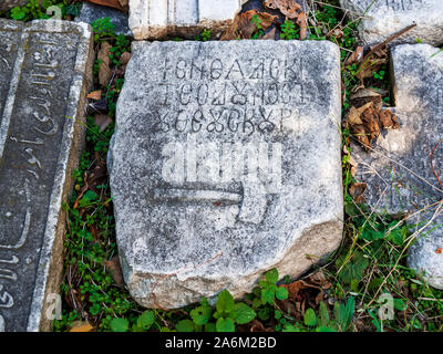 Fragment of an antique carved stone block with an inscription in ancient language and the bas-relief of a hammer. Antique artifact outdoors. Stock Photo