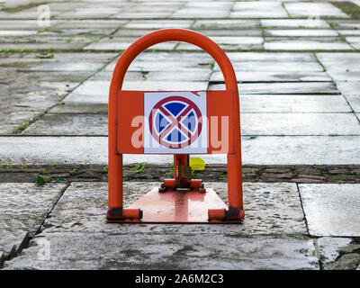 Portable road sign no stopping or parking on an orange car parking lock device over wet concrete slabs near building. Traffic rules,  prohibitory sign Stock Photo