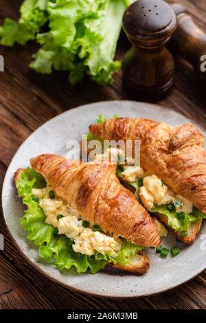 Croissant egg sandwich with green lettuce salad on plate on wooden table. Top view. Healthy tasty breakfast sandwich Stock Photo