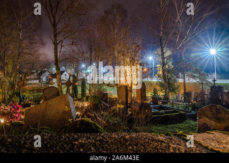 Autumn evening of All Saints' Day at the cemetery in Trakai, Lithuania. Flowers and candles placed on graves to honor deceased relatives Stock Photo