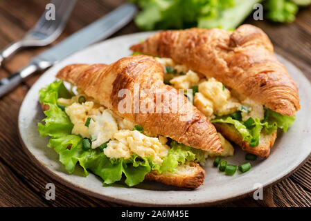 Breakfast croissant sandwich with scrambled eggs and green lettuce salad Stock Photo