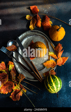 Autumnal table setting with bright yellow leaves and pumpkins on stone background with copy space Stock Photo