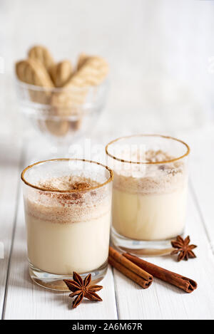 Eggnog in glass cups with a delicate foam, spices and a cinnamon stick Stock Photo