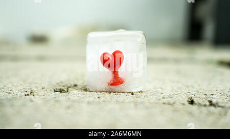 Red elastic rubber heart frozen in an ice cube melting in the sun Stock Photo