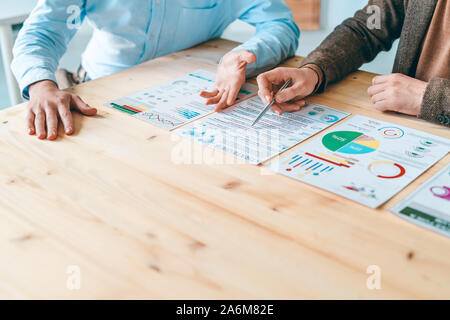 Two young businessmen sitting by wooden table while discussing documents Stock Photo