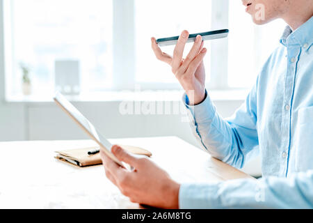 Young designer using touchpad and holding smartphone by his mouth Stock Photo