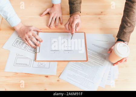 Hands of two programmers discussing one of papers with software application Stock Photo