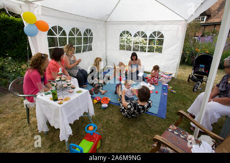 two year old birthday party with mothers sat watching child opening presents in garden, England Stock Photo