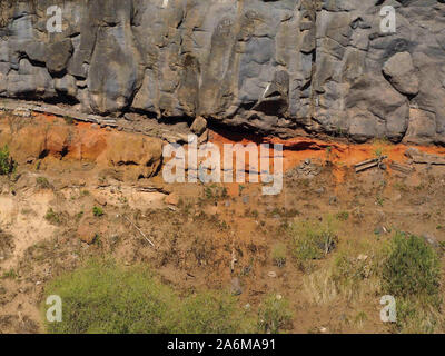 different coloured volcano rock layers on top of each other. Above black vertical ashlars, below ferruginous red loose volcanic rock and below then tu Stock Photo