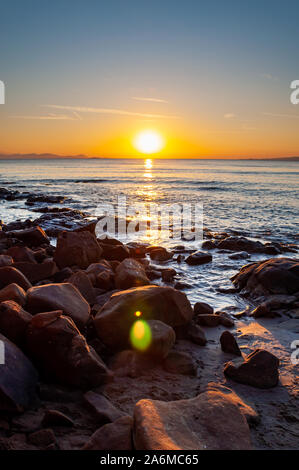 Scenic rocky beach Cala Violina landscape at the sunset. The sun is going down behind the horizon. Tyrrhenian Sea bay at the sunset. Province of Grose Stock Photo