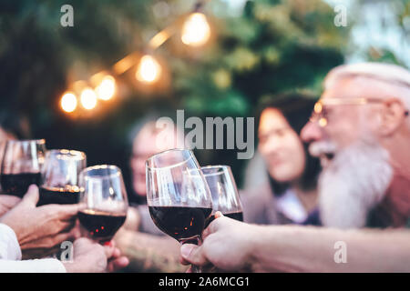 Happy family eating and drinking red wine at dinner barbecue party outdoor - Mature and young people cheering and toasting with wineglass on rooftop Stock Photo