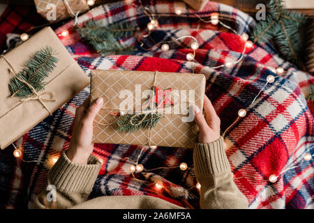 View of young woman wrapped into warm checkered plaid holding giftbox Stock Photo