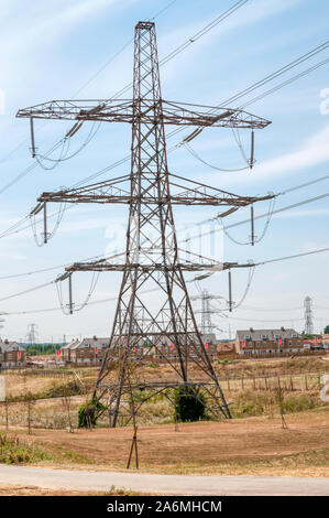 A traditional lattice transmission tower or electricity pylon carries an overhead line across a housing area at the Ebbsfleet Garden City development. Stock Photo