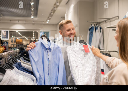Happy young man showing two shirts to his girlfriend while choosing new one Stock Photo