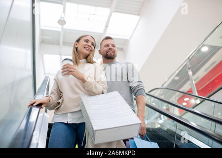 Young couple with paperbags moving down on escalator during shopping Stock Photo