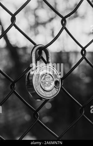 Closed padlock hanging on a fence - symbol of love - black & white Stock Photo