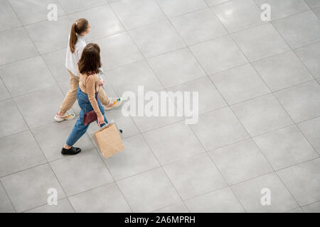 Two female customers in casualwear walking down large contemporary trade center Stock Photo