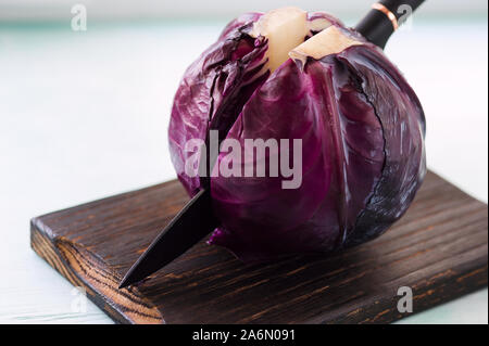 Fresh red cabbage on cutting board cut in half with a knife. Preparing  for slicing for cooking purple cabbage salad or coleslaw. Food concept. Stock Photo