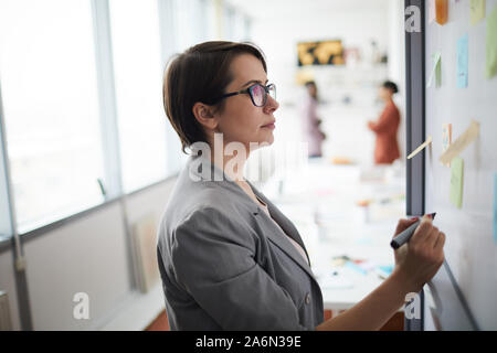 Side view portrait of modern businesswoman writing on whiteboard in office, copy space Stock Photo