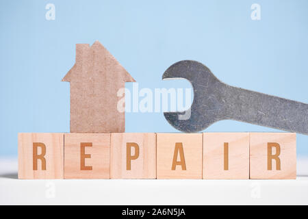 Abstract cardboard house next to a wrench, wooden cubes. Real estate repair concept. Close up. Stock Photo