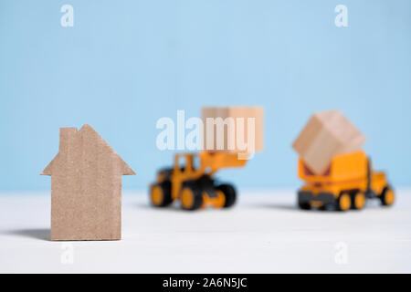 Abstract cardboard house next to construction equipment. The concept of the start of construction. Close up. Stock Photo