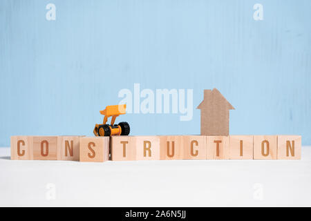Abstract cardboard house next to wooden cubes with inscriptions and construction equipment. Construction concept. Close up. Stock Photo