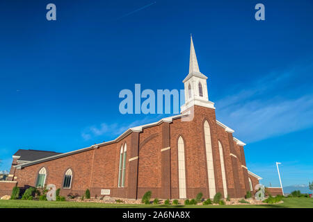Sunny day view of a church with white steeple and vibrant blue sky background Stock Photo