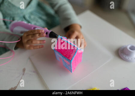 Cute little girl makes a plastic house, draws parts with a 3D pen. STEM and STEAM education. Development, modeling, education, design with hot plastic Stock Photo