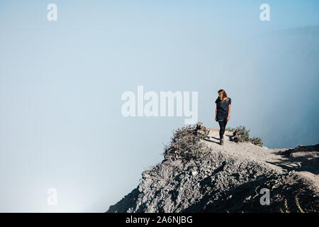Young woman in protective mask on summit of active volcano Kawah Ijen above crater acid lake with poisonous fume. Popular travel destination. Stock Photo