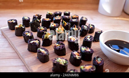 presentation of vegetarian sushi rolls on a light wood tray and countertop next to a white bowl of dipping sauce Stock Photo