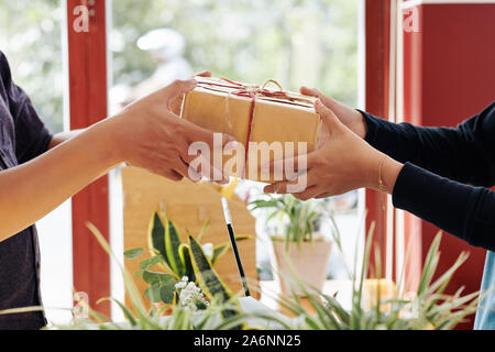 Hands of customer buying wrapped birthday present in flower shop Stock Photo