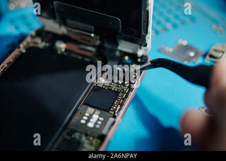 Close-up image of smartphone repairman using tweezers to remove antenna cable when trying to get access to the speaker Stock Photo