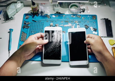 Hands of repairman exchanging smartphone screen with many cracks with the new one Stock Photo