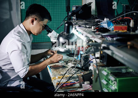 Repairman using microscope when fixing small details in smartphone Stock Photo