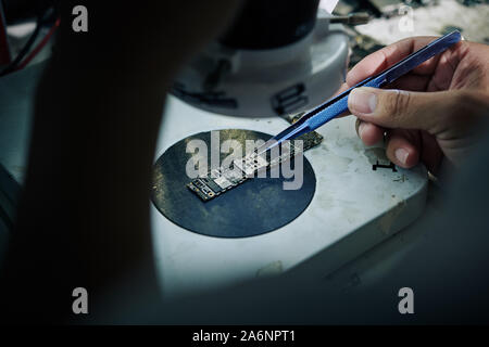 Repairman using tweezzers when putting smartphone random access memory on microscope stage Stock Photo