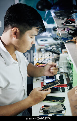 Young Asian repairman opening small drawer when searching for details for broken smartphone Stock Photo