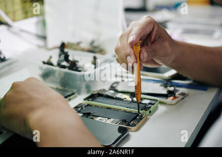 Hands of repairman using pentalob screwdriver when removing smartphone battery Stock Photo