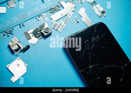 Cracked modern smartphone, broken camera, metal brackets and screws, view from above Stock Photo