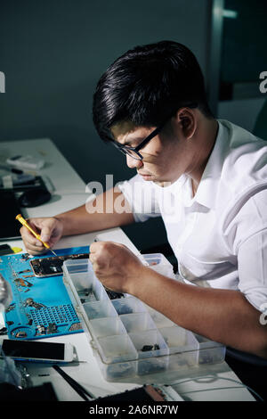 Professional Vietnamese repairman concentrated on fixing smartphone Stock Photo