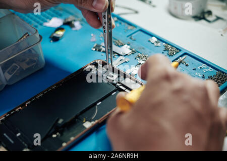 Hands of repairman using tweezers when fixing smartphone camera Stock Photo