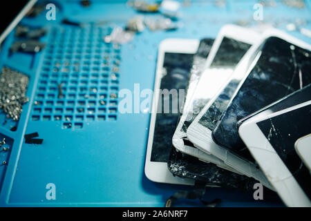 Smashed and cracked smartphone screens on table in repair workshop, selective focus Stock Photo