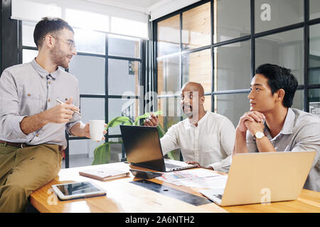 Cheerful business colleagues gathering at meeting room and discussing new project the are working on Stock Photo